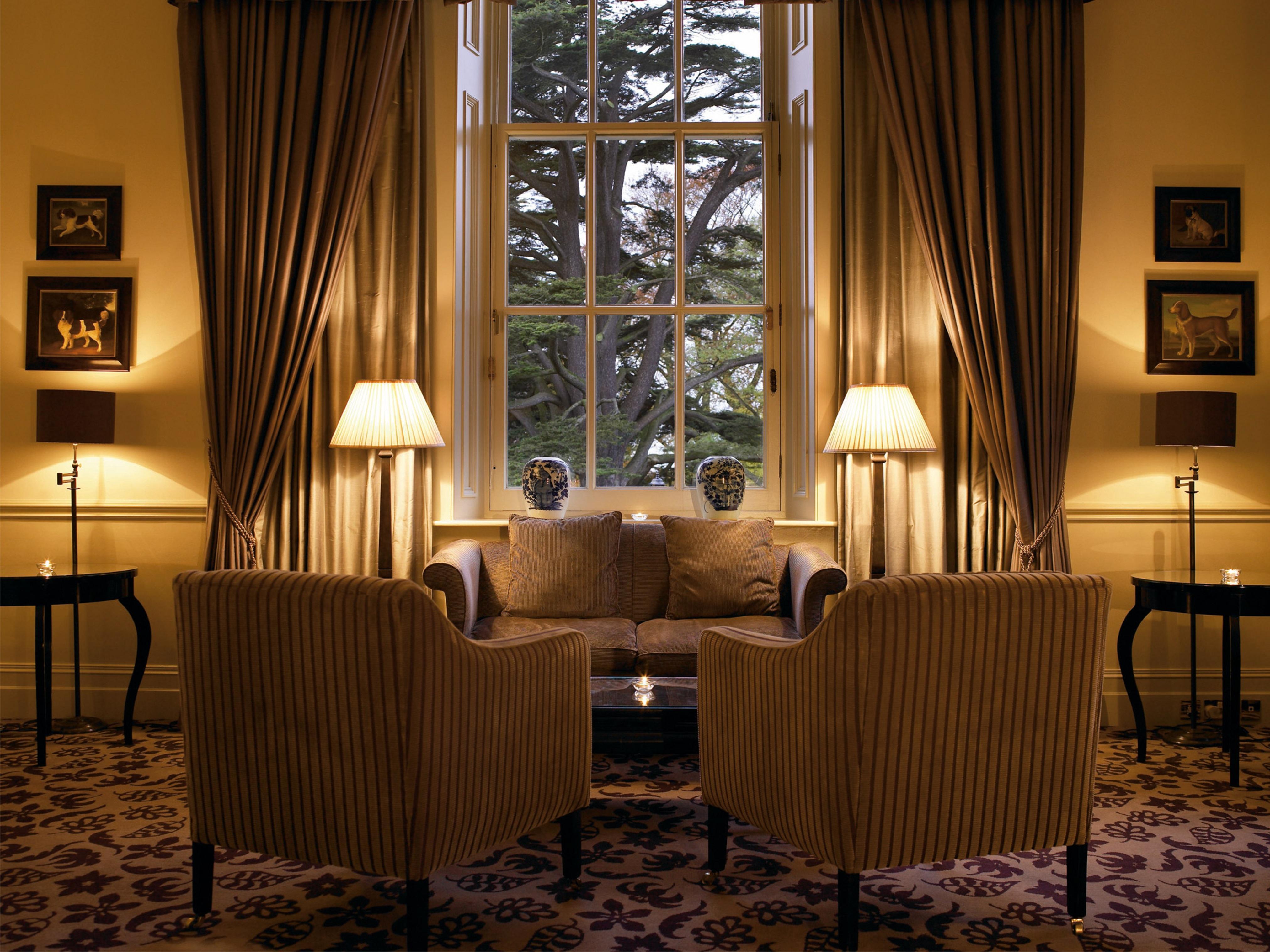 Macdonald Bath Spa Hotel Екстер'єр фото The photo shows a cozy and elegant sitting area. There are two upholstered armchairs facing a small sofa, all arranged around a central coffee table. Soft lighting is provided by two lamps with white shades, one beside each chair. The window behind t
