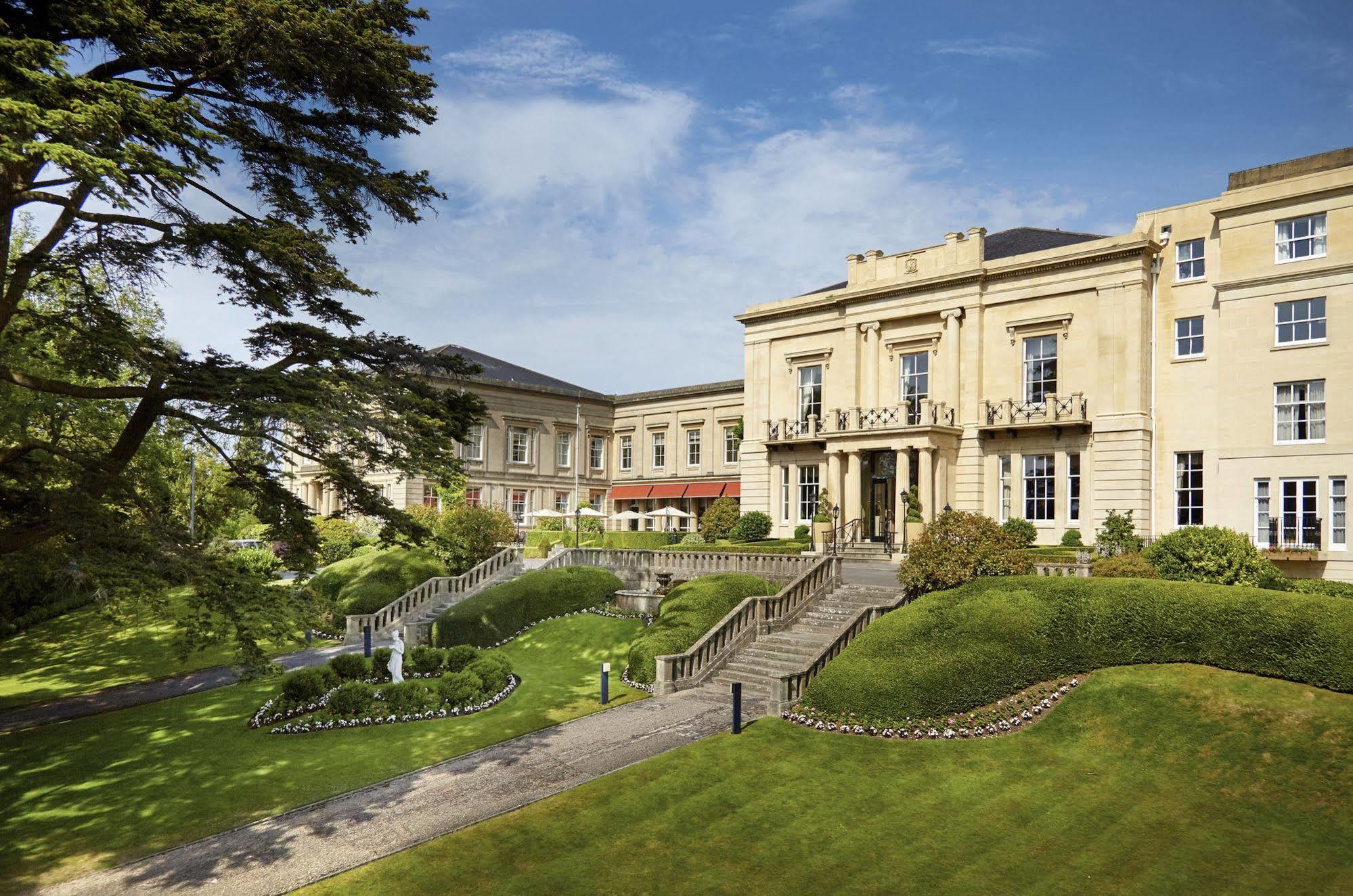 Macdonald Bath Spa Hotel Екстер'єр фото The photo shows a grand building, likely a hotel or estate, surrounded by well-manicured gardens and lawns. The architecture appears elegant, with multiple stories and large windows. There are steps leading up to the entrance, and the setting include